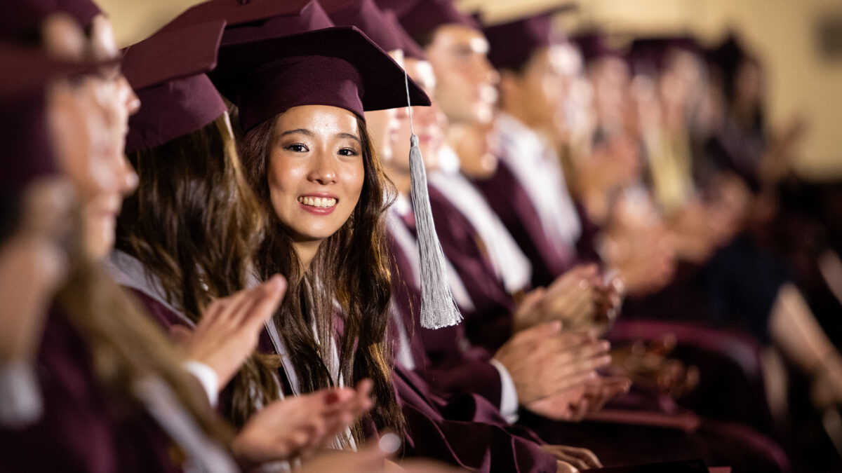 A college graduate smiles at the camera during her graduation ceremony.
