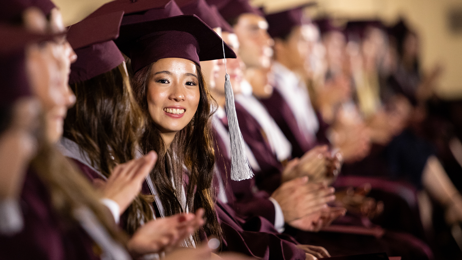 A college graduate smiles at the camera during her graduation ceremony.
