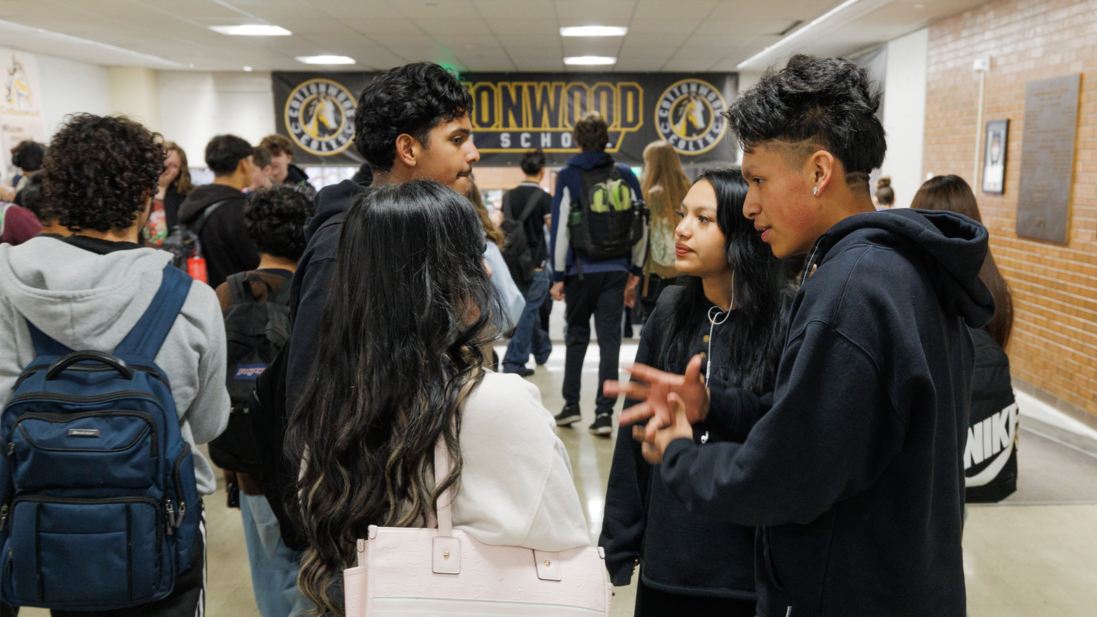 A group of high school students are talking to each other in the school hallway.