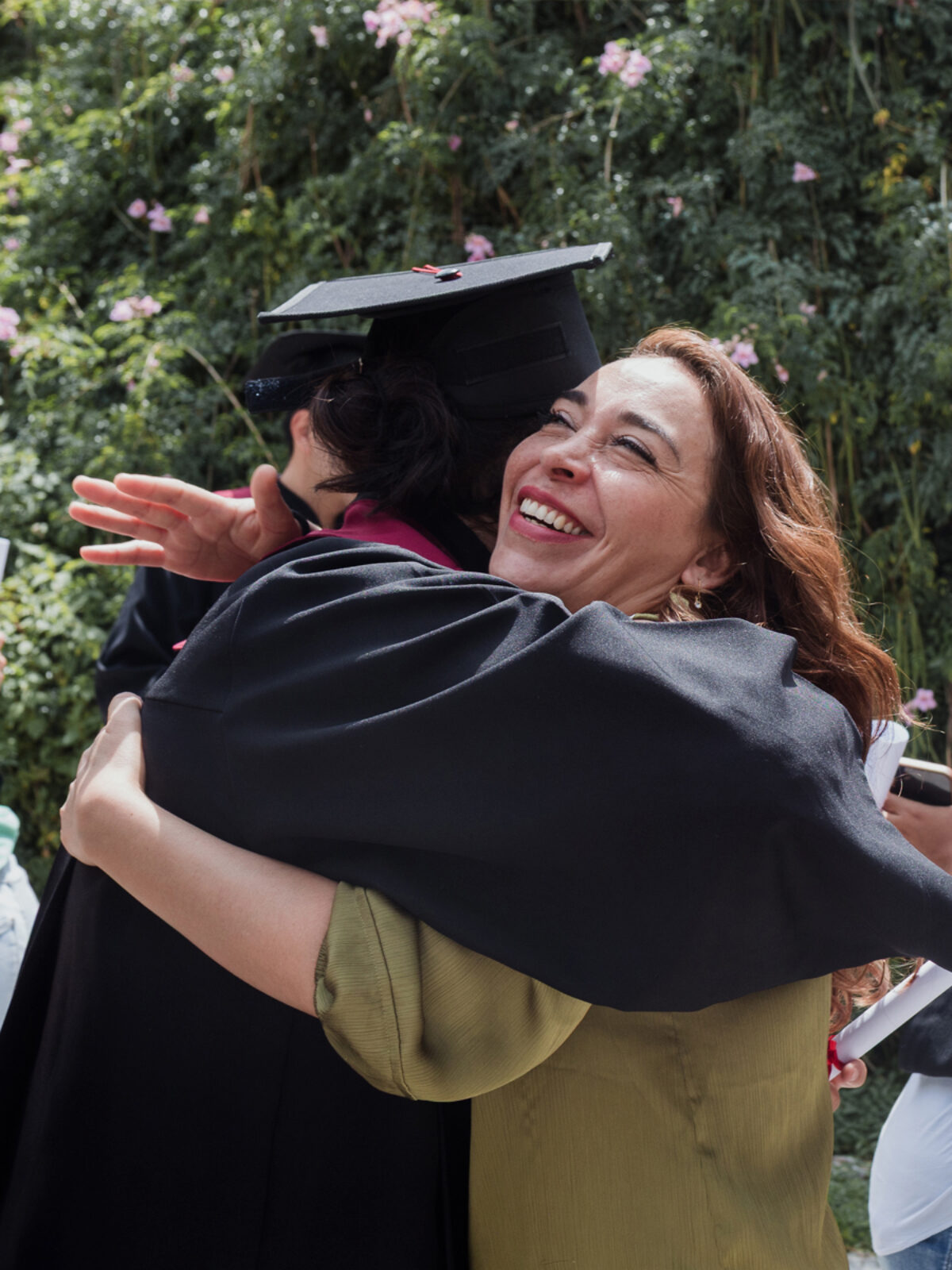 A parent hugs their student who's wearing a cap and gown and holding a diploma.