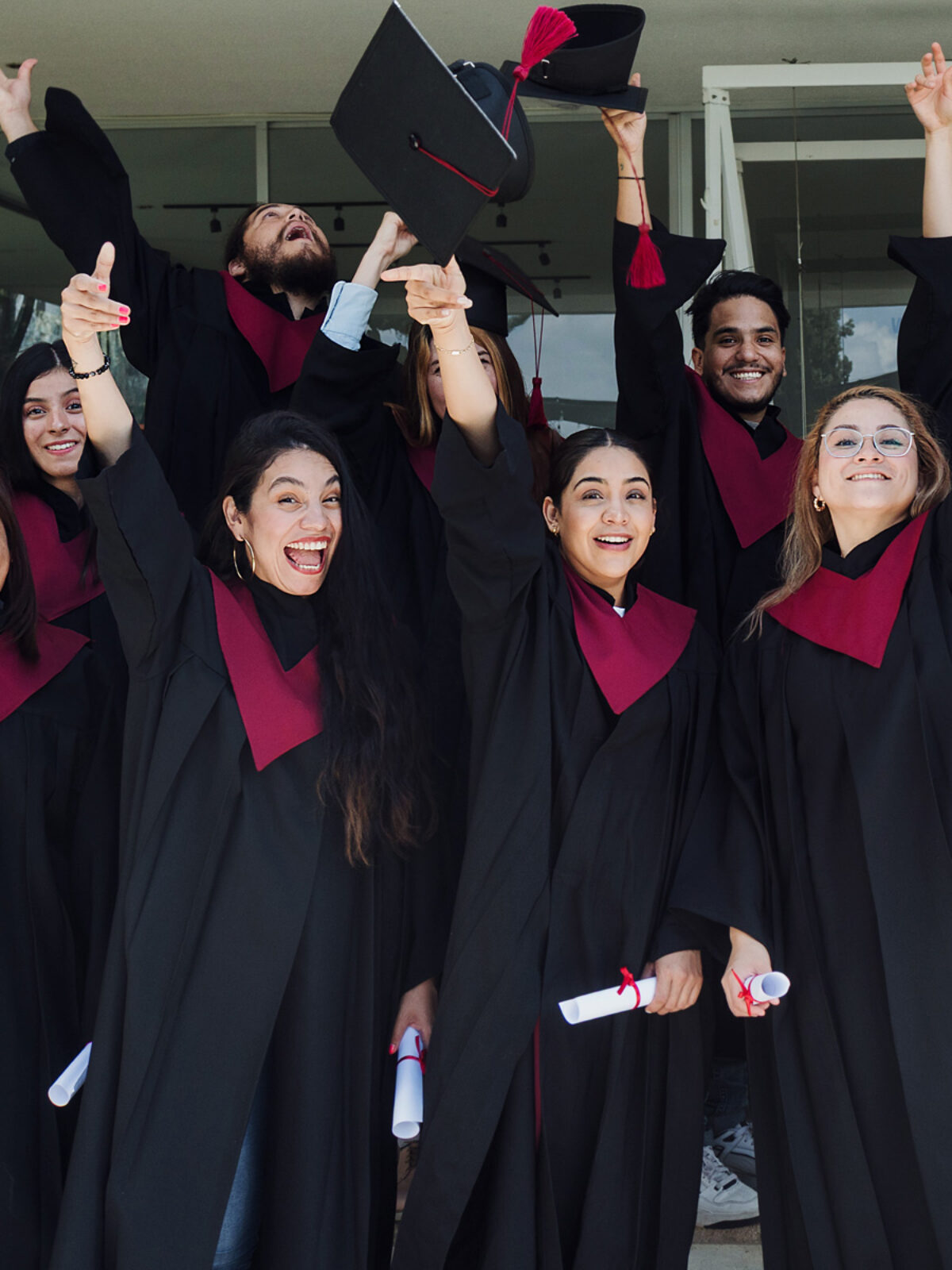A group of college graduates smile at the camera as they toss their caps.