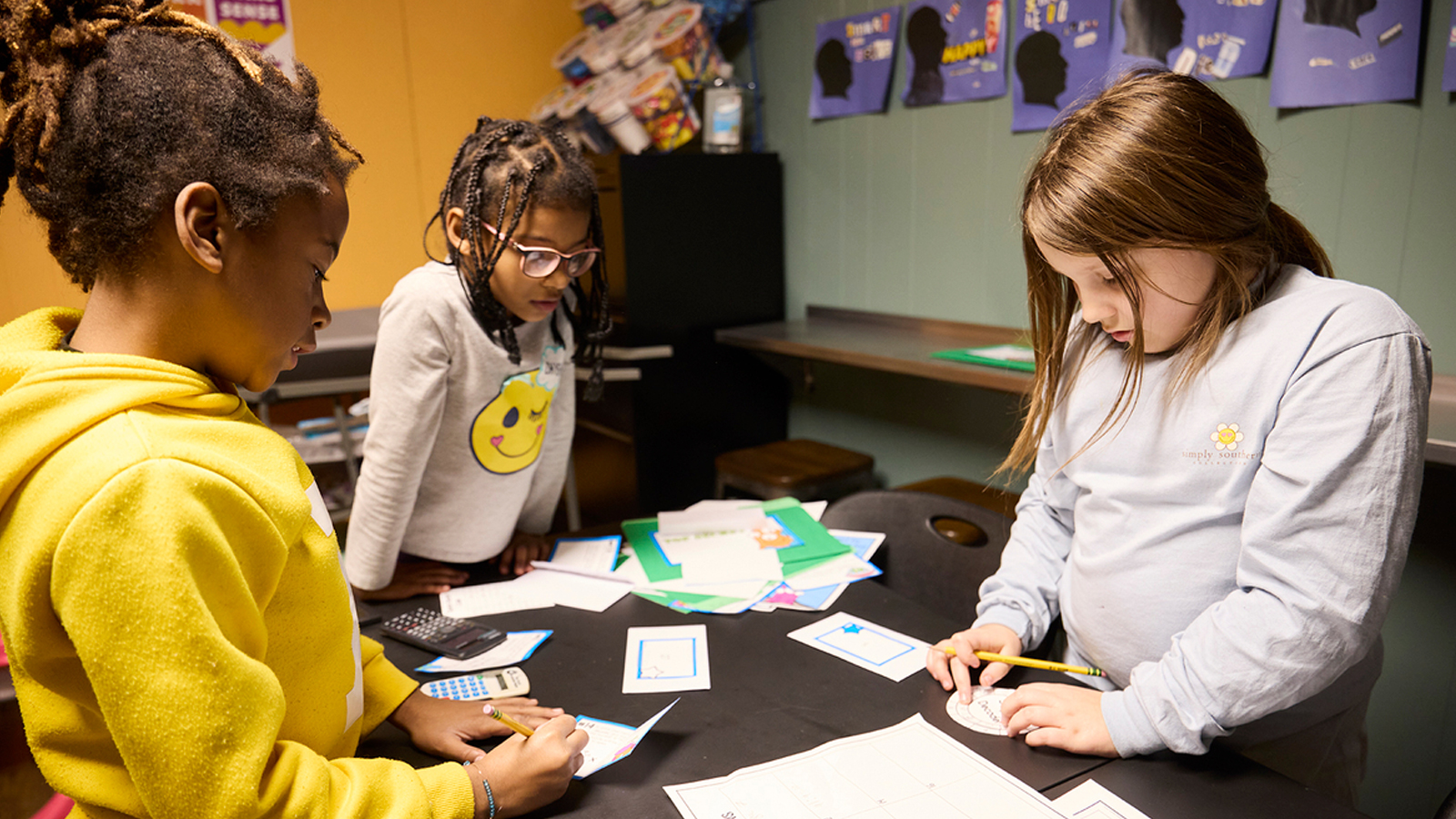 A group of young students stand around a table working on a project together.