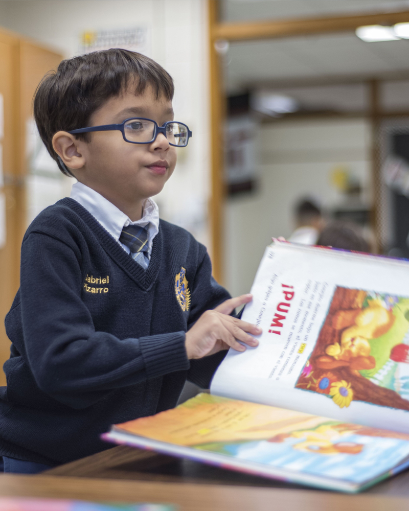 A young boy sits at a desk with a picture book open in front of him