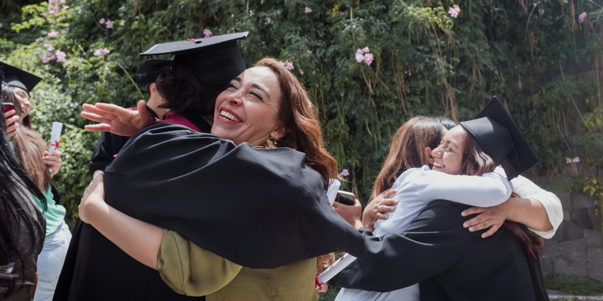A parent hugs their student who's wearing a cap and gown and holding a diploma.