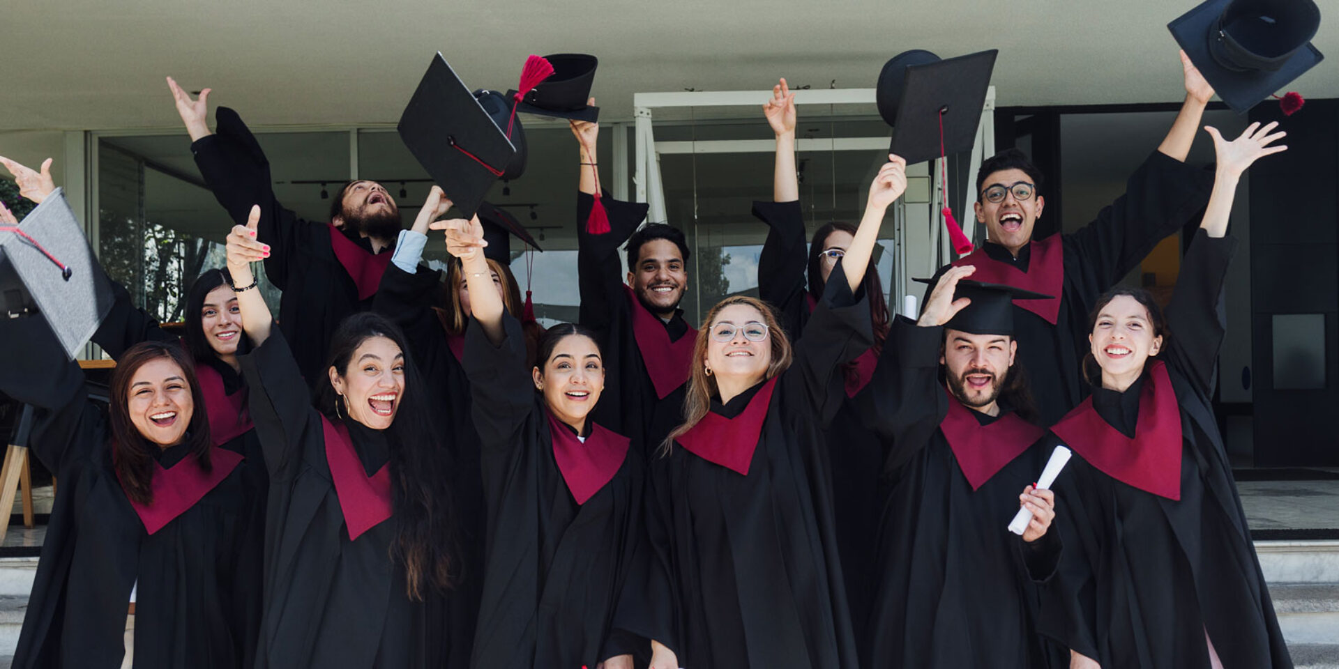 A group of college graduates smile at the camera as they toss their caps.