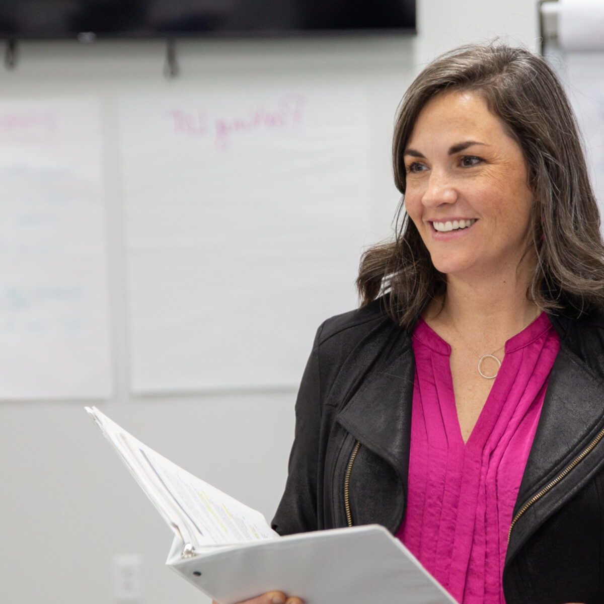 Meghan Smith, director of the Center for Postsecondary Success at Cradle to Career Network member Spartanburg Academic Movement, stands at the front of a room holding a binder open.