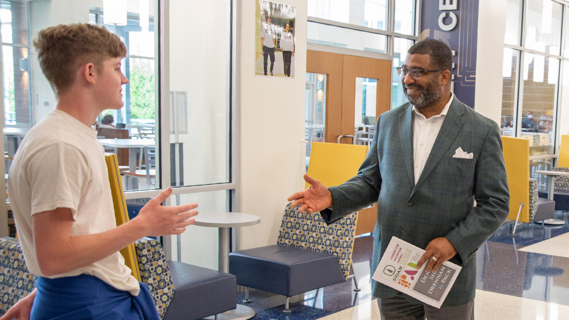 Dr. Russell W. Booker, CEO of Spartanburg Academic Movement, stands with his hand outreached to shake a high school student's hand. They're standing in the school lobby.