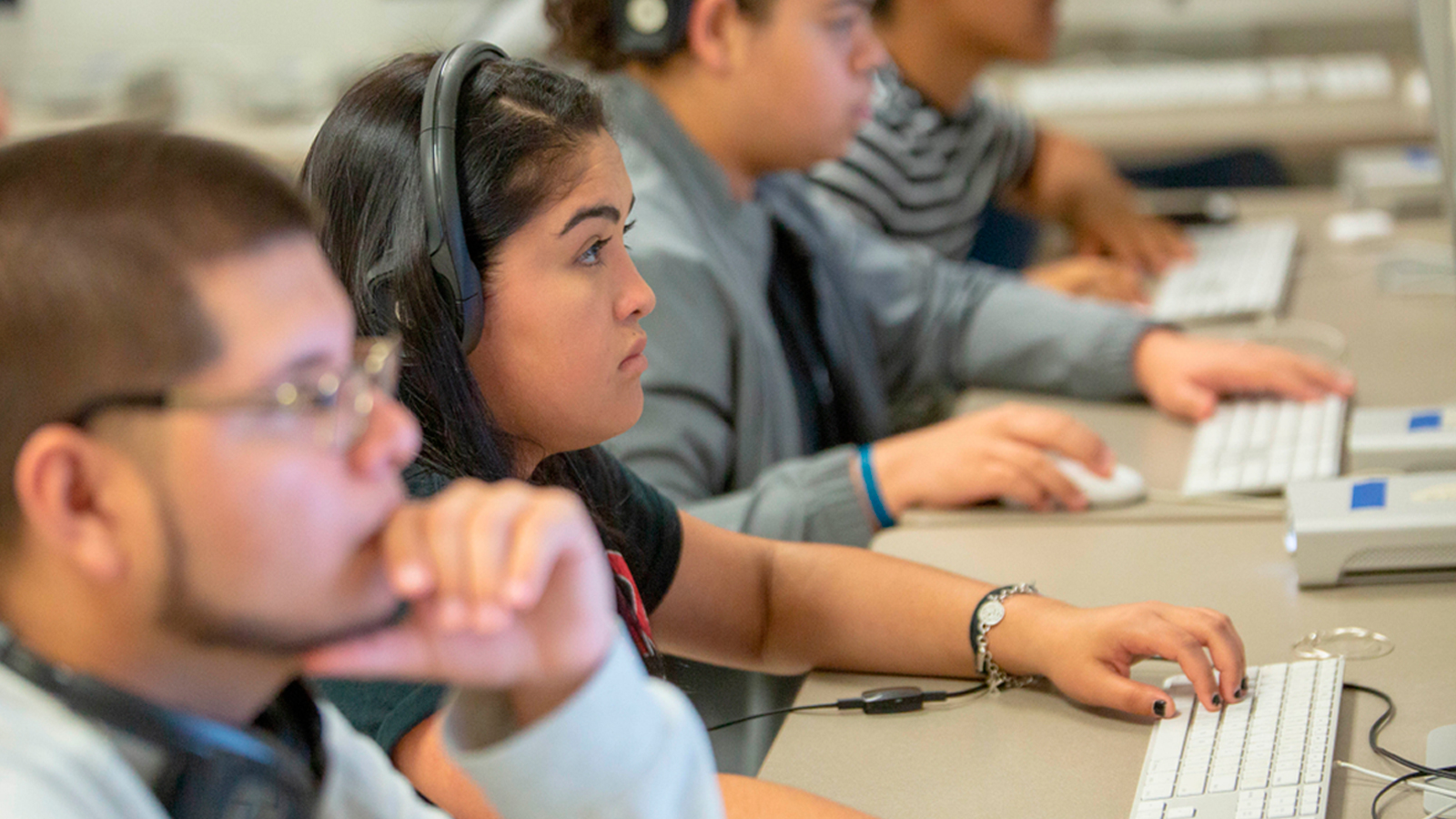 A row of college-aged students sit at computers.